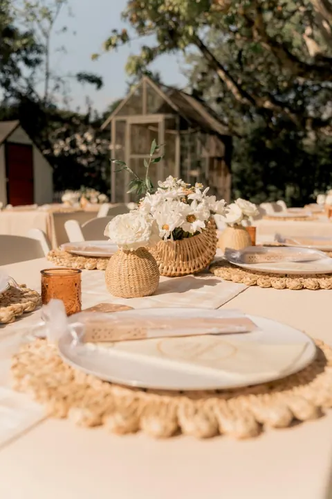 Outdoor table with ivory linen, woven chargers and white flowers